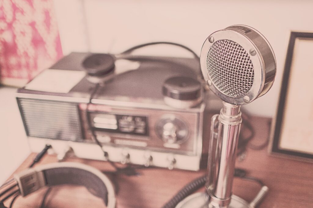 Vintage radio, broadcast microphone and headphones on a wooden table.