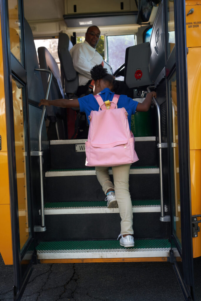 Elementary student uses the handrails while boarding a yellow school bus.