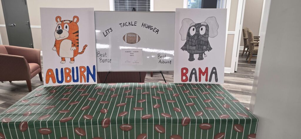 Union State Bank food drive header showing the Cedar Bluff office’s hand-drawn Alabama and Auburn display and a football tablecloth.
