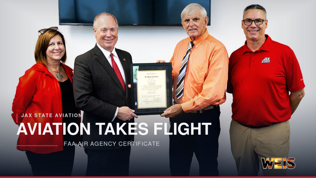 Four representatives display an FAA Air Agency Certificate for the Jax State aviation program at Merrill Hall.