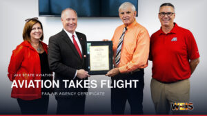 Four representatives display an FAA Air Agency Certificate for the Jax State aviation program at Merrill Hall.
