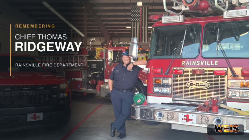 ainsville Fire Chief Thomas Ridgeway stands beside department fire trucks in a memorial news header.