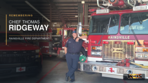 ainsville Fire Chief Thomas Ridgeway stands beside department fire trucks in a memorial news header.
