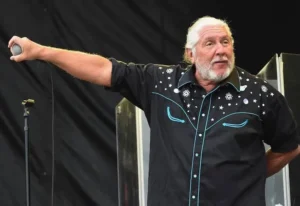 Doug Gray of The Marshall Tucker Band holds a microphone toward the audience during a performance.