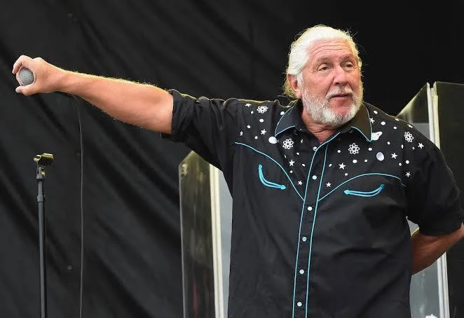 Doug Gray of The Marshall Tucker Band holds a microphone toward the audience during a performance.