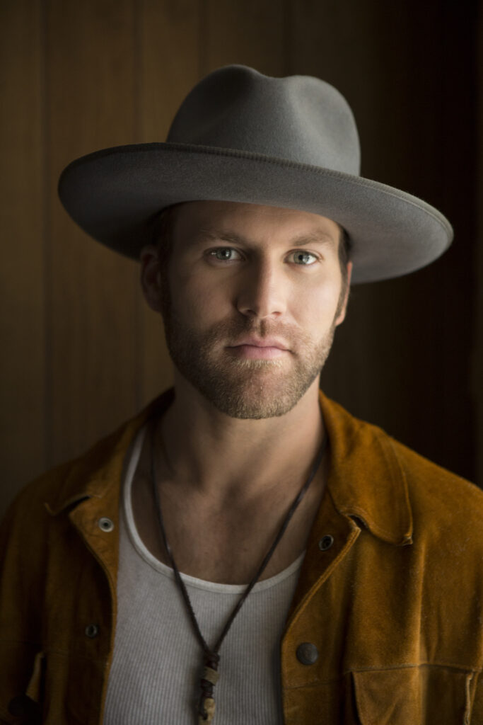 Drake White wearing a gray wide-brimmed hat and a brown jacket.