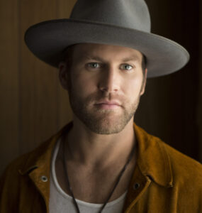 Drake White wearing a gray wide-brimmed hat and a brown jacket.