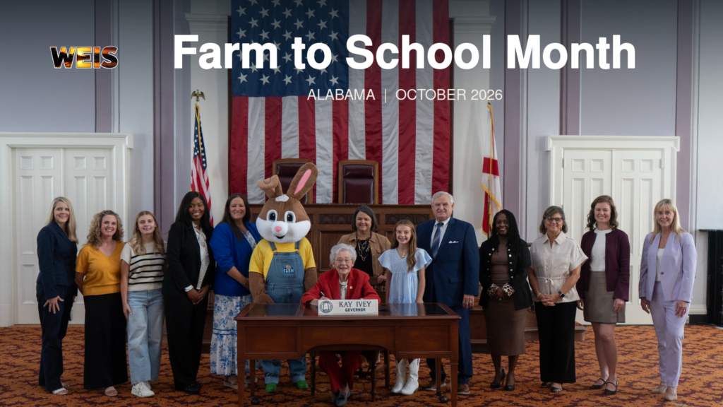 Governor Kay Ivey poses with a group in the supplied Farm to School Month photo, with the headline and WEIS branding.