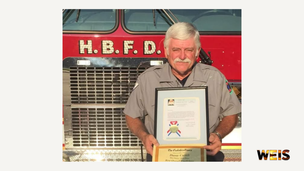 Danny Coffelt holding a framed certificate in front of a Hokes Bluff fire truck, with the WEIS logo.