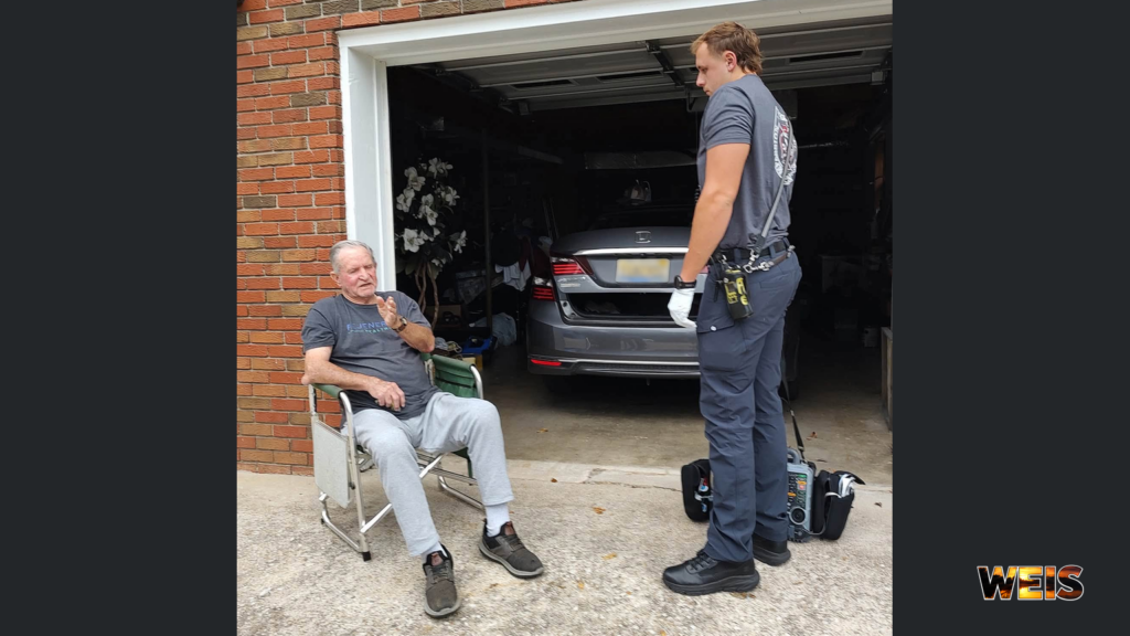 Jacksonville ambulance crew member standing beside a seated man outside a residential garage.