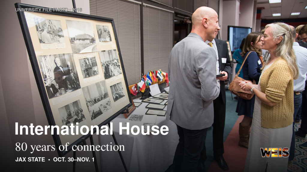 Jax State International House reunion attendees beside a historical photo display at the 2016 reunion, with 80th anniversary headline.