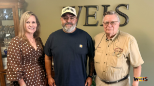 Loblolly Fest announcement photo showing three people posing at WEIS Radio with the station’s wall sign behind them.