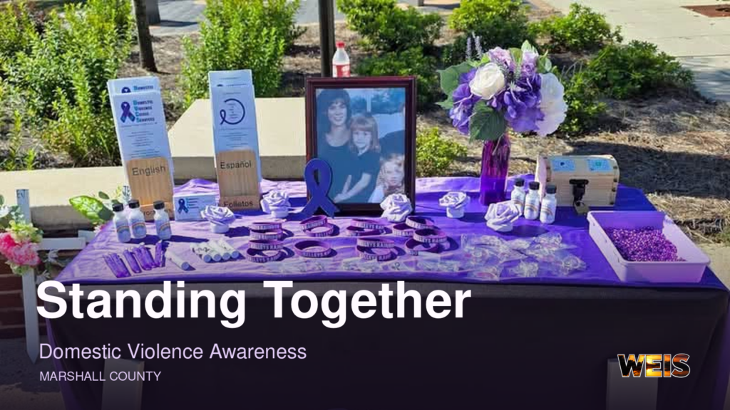 Domestic violence awareness display with purple materials, flowers, and a framed photograph, with WEIS branding.