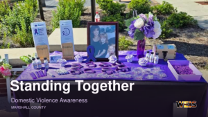 Domestic violence awareness display with purple materials, flowers, and a framed photograph, with WEIS branding.